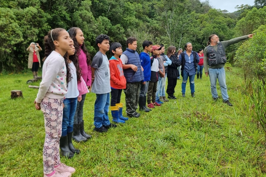 Foto de adultos dando explicações para crianças sobre a floresta à sua frente