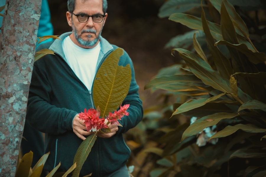Foto de homem em pé, segurando uma grande folha verde e pequenas flores vermelhas