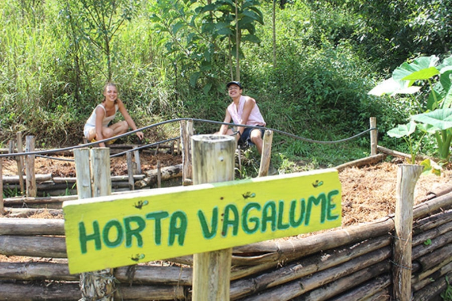 Foto de um homem e uma mulher ao fundo de uma placa com a inscrição Horta Vagalume