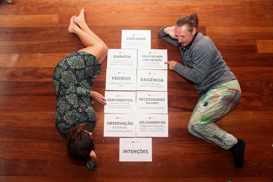 Foto de homem e mulher deitados no chão, em sentidos opostos, em volta de folhas de papel com palavras escritas