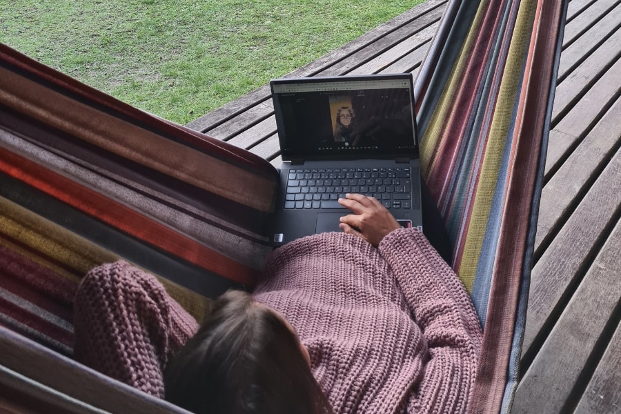 Foto de uma mulher, mexendo em um notebook, deitada numa rede