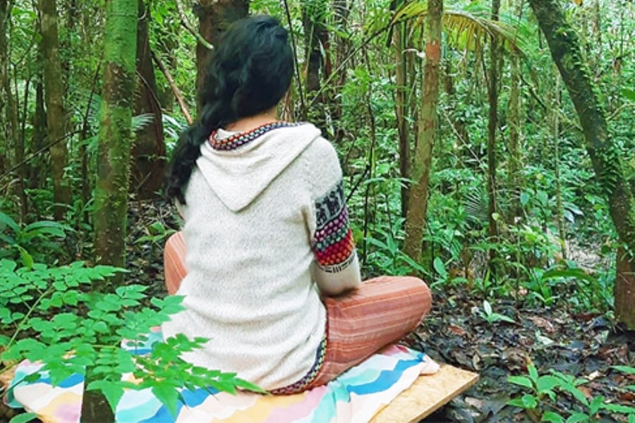Foto de moça de costas sentada em almofadas no meio da floresta