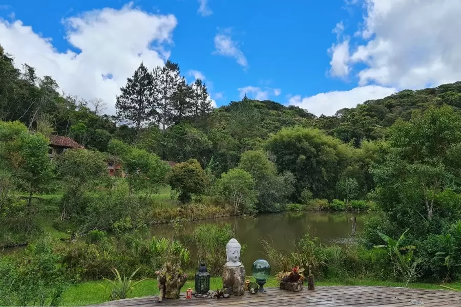 Foto de um lago, com algumas imagens budistas, flores e velas às margens