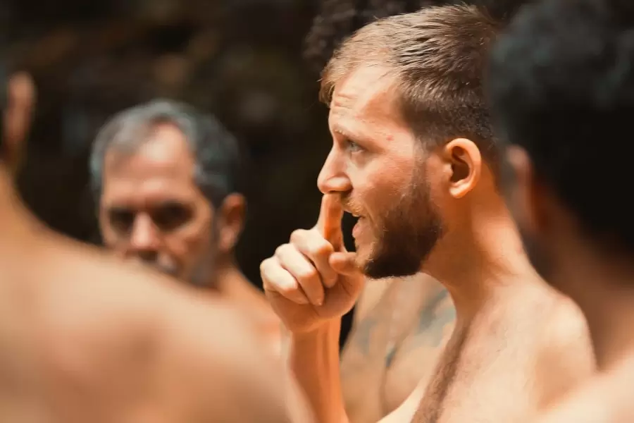 Foto de homem em pé, sem roupa e dando explicações parra outros homens