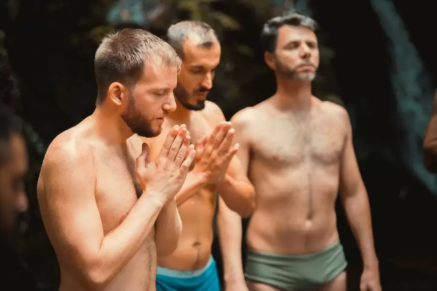 Foto de homens em pé, sem roupa e de olhos fechados, ouvindo explicações