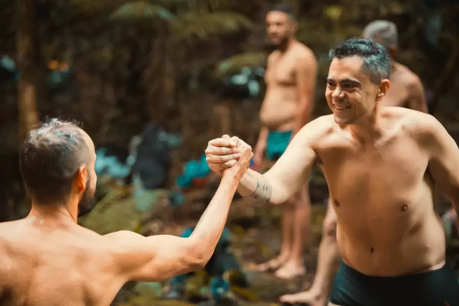 Foto de homens se cumprimentando e sorrindo, com outros homens ao fundo