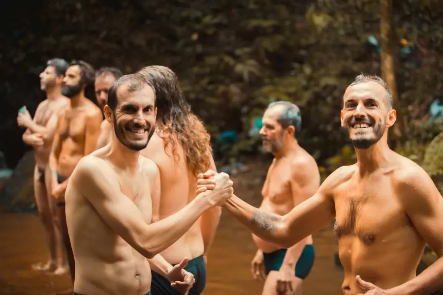 Foto de homens se cumprimentando e sorrindo, com outros homens ao fundo