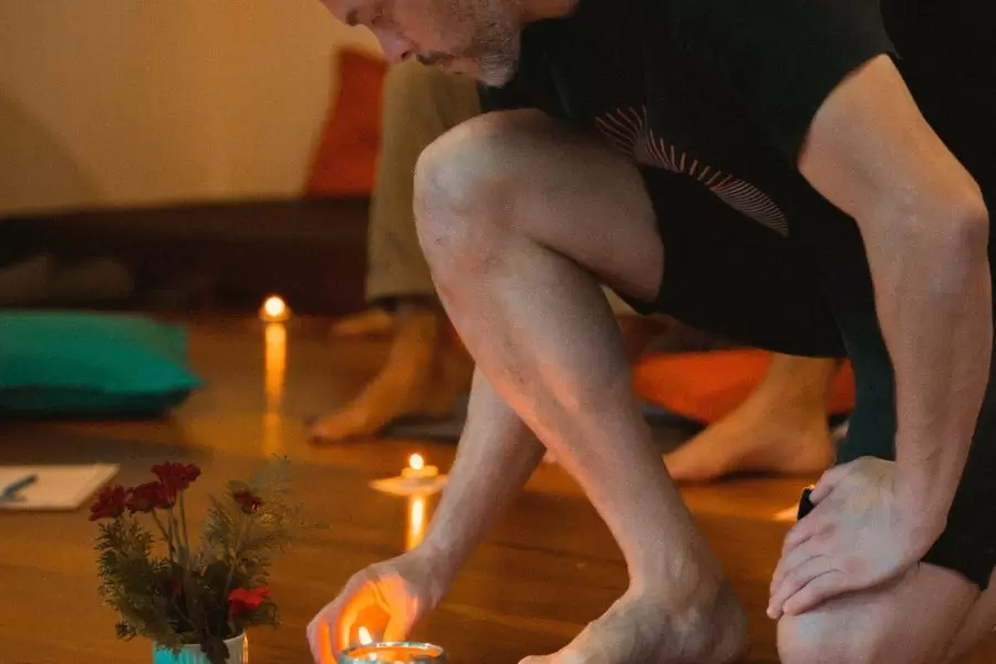 Foto de homem acendendo uma vela, num suporte, no chão de uma sala