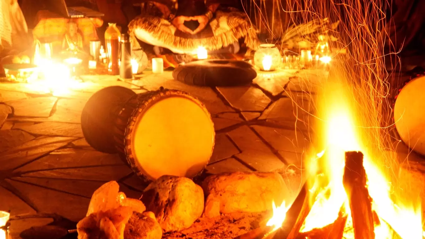Foto de tambores deitados no chão, com uma fogueira, muitas velas e uma pessoa sentada ao fundo