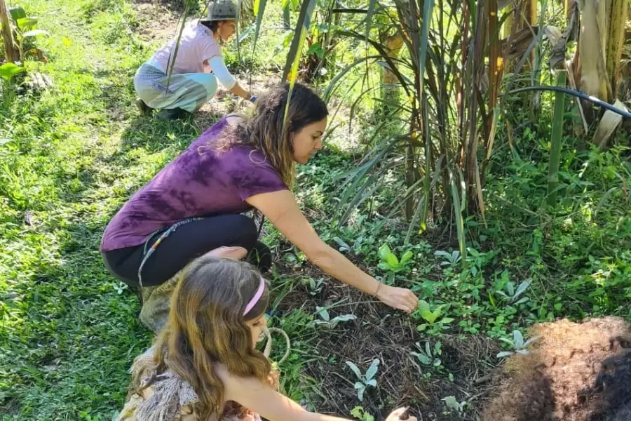 Foto de duas mulheres e uma menininha agachadas, mexendo na terra