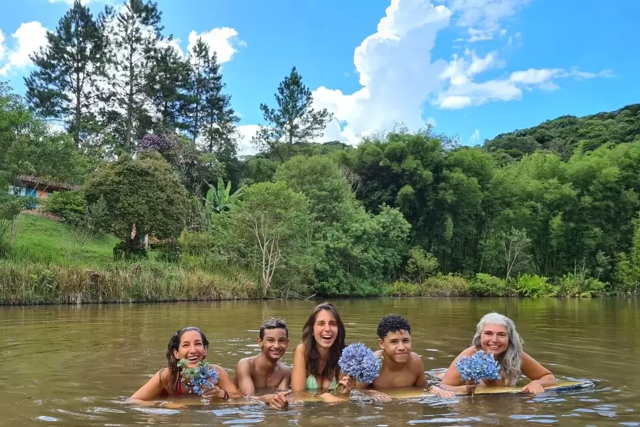 Foto de cinco pessoas mergulhadas num rio, com vegetação ao fundo. As três mulheres seguram pequenos buques de flores.