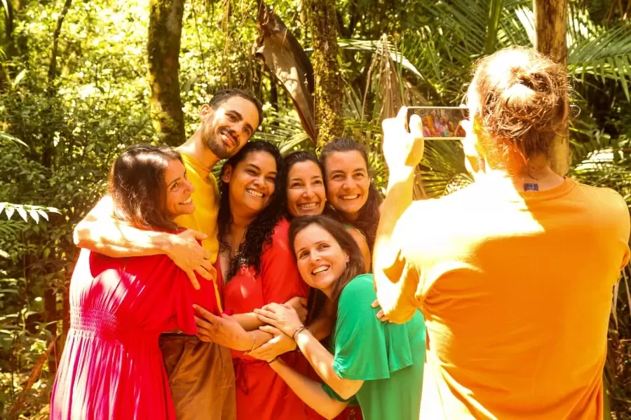 Foto de várias pessoas abraçadas e sorrindo para uma moça que tira uma foto com o celular