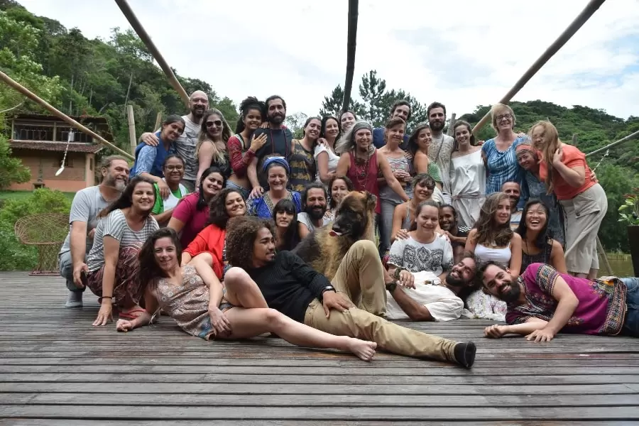 Foto de várias pessoas alegres, todas juntas, posando para a foto, num grande deck de madeira