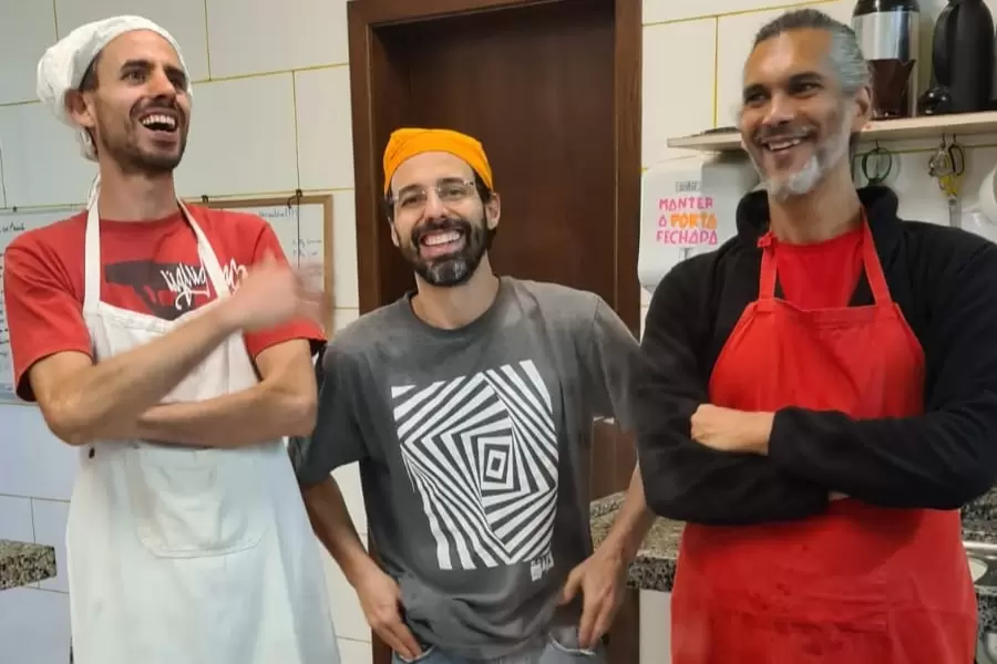 Foto de 3 homens, 2 de avental, alegres, numa cozinha
